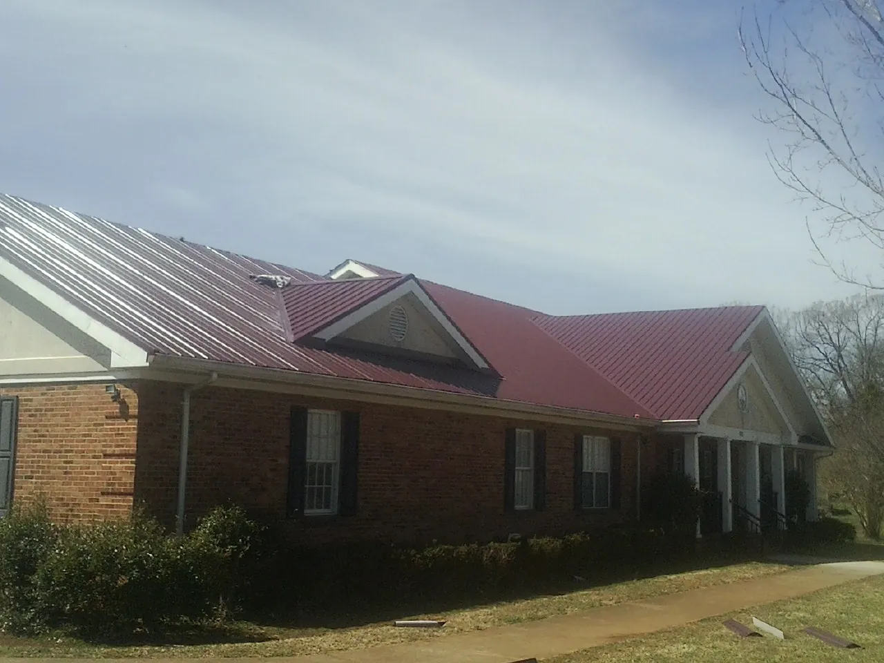 Red metal roof with gabled entries on a long brick building, from a Hail Damage Roof Repair job in Stirling