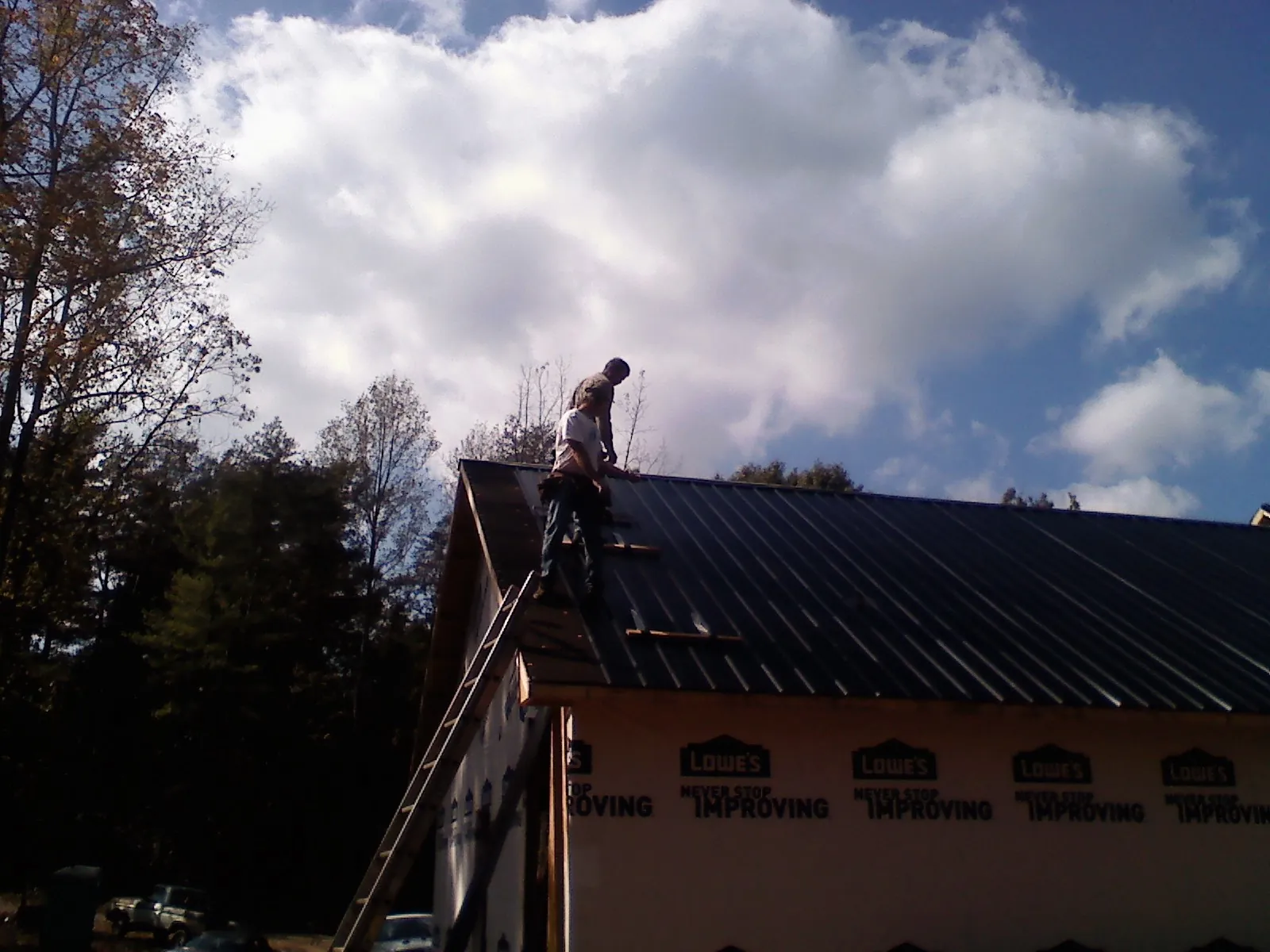 Roofer fastening dark metal panels high against a cloudy sky, from a Roof Inspection job in Stirling