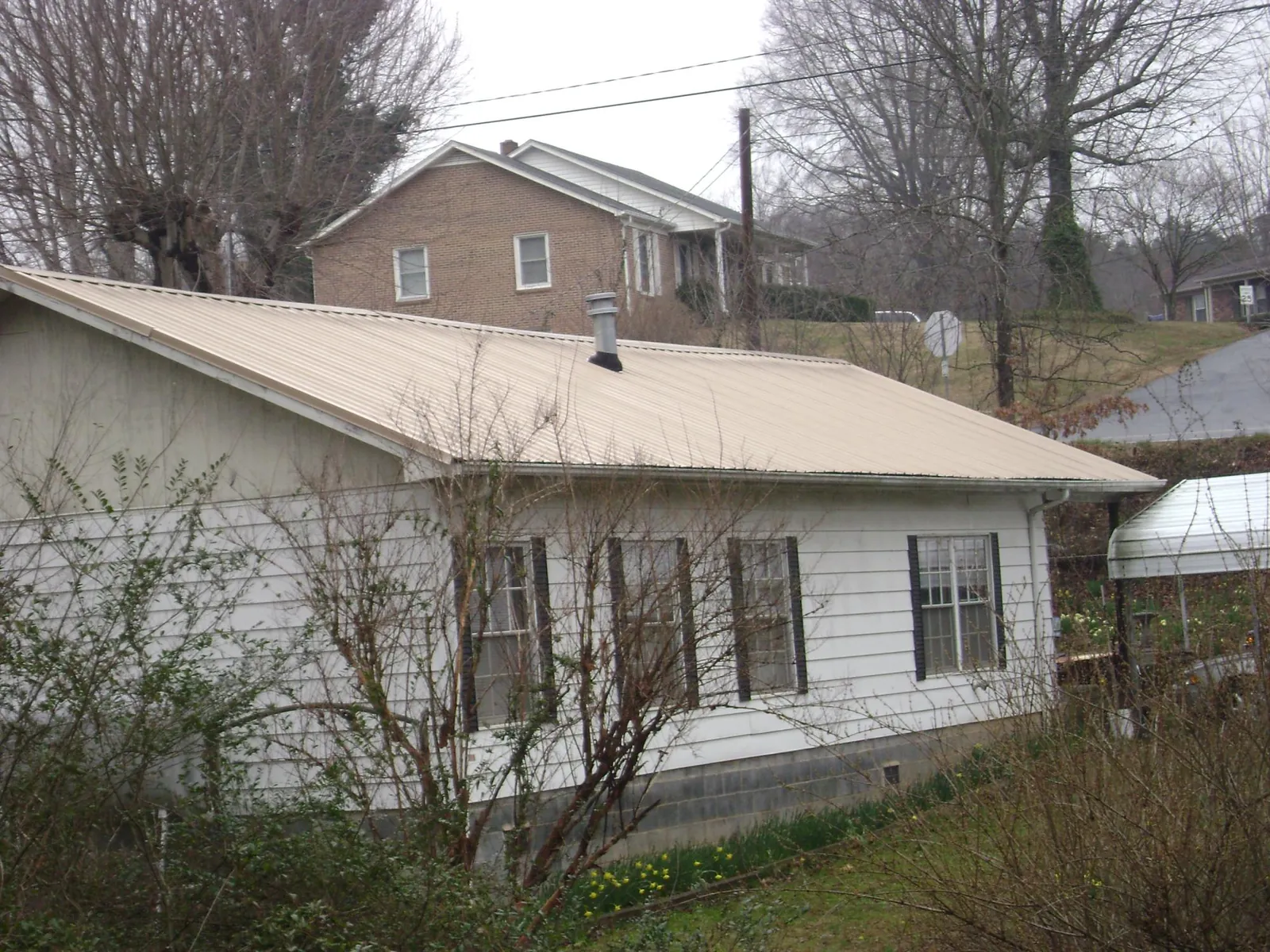 Tan metal roof on a white sided house set into a hillside — Commercial Roofing by Roofing Brothers in Stirling